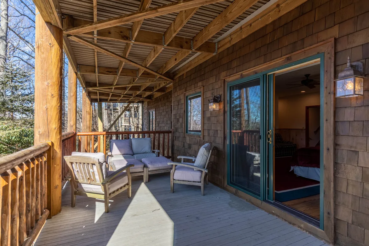 This image showcases a wooden deck with comfortable outdoor seating and a sliding glass door, set against a peaceful natural backdrop. The deck appears inviting for both people and pets to relax and enjoy the fresh mountain air after a walk.