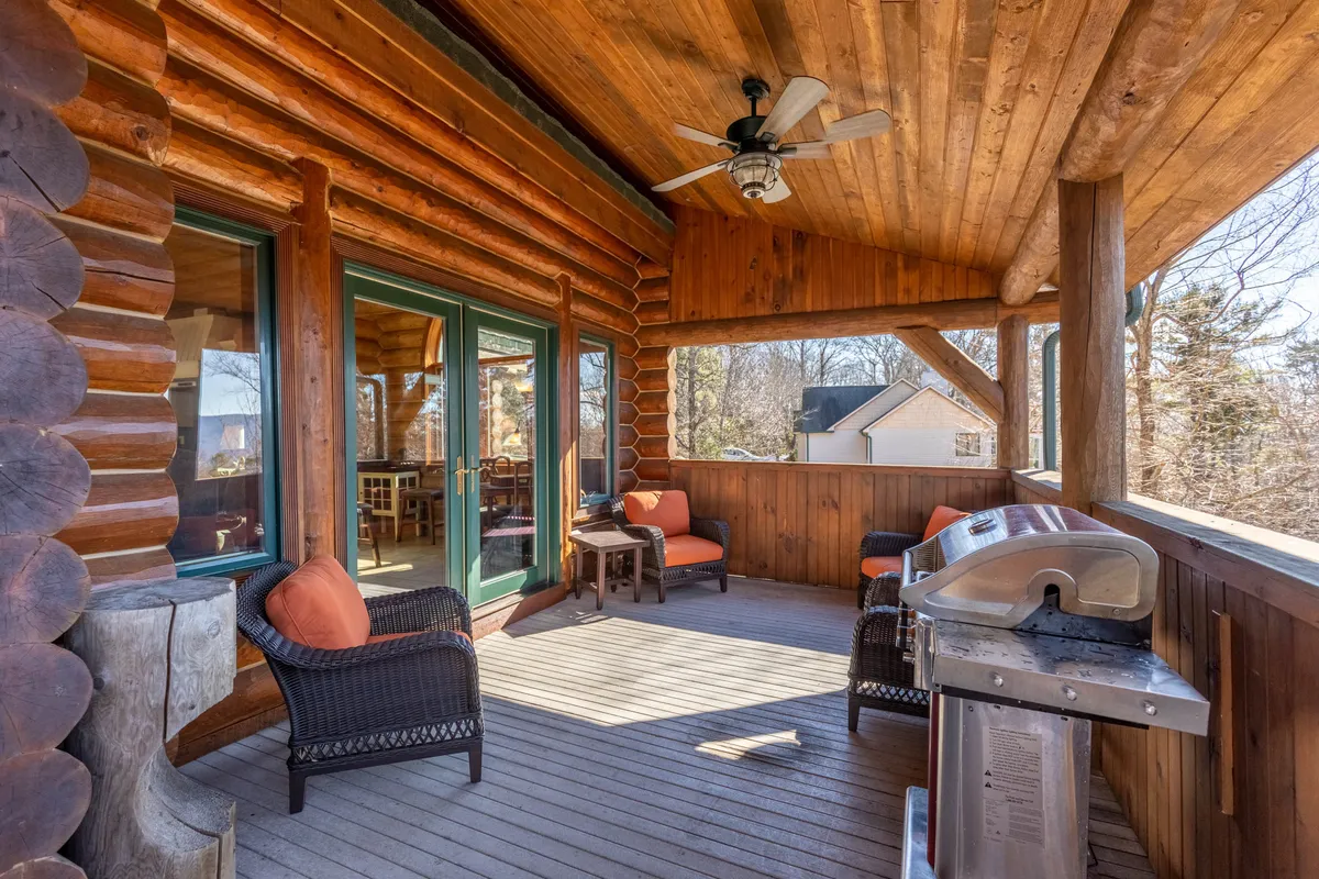 An exterior deck with a wooden log structure, outdoor seating, and a grill set against a mountain backdrop. The scene suggests summer barbecues and alfresco dining, with the grill as a central feature and cozy gathering spots.