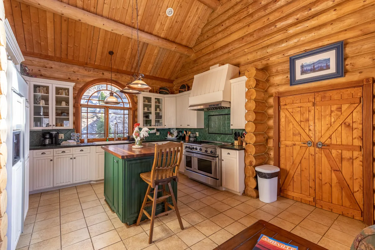 A close-up of the kitchen’s core functional zone, highlighting a central island with bar stools, wooden cabinetry, an arched window for natural light, and a prominent cooking range. The arrangement invites participation and conversation while cooking, showcasing the kitchen as an inviting, interactive space.