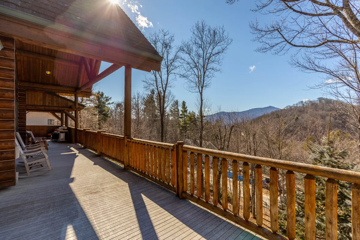 This exterior image captures a wooden deck overlooking a breathtaking mountain view, surrounded by lush trees. Comfortable seating invites guests to relax, while the expansive vista provides a sense of tranquility and a perfect spot for sunset cocktails or morning coffee.