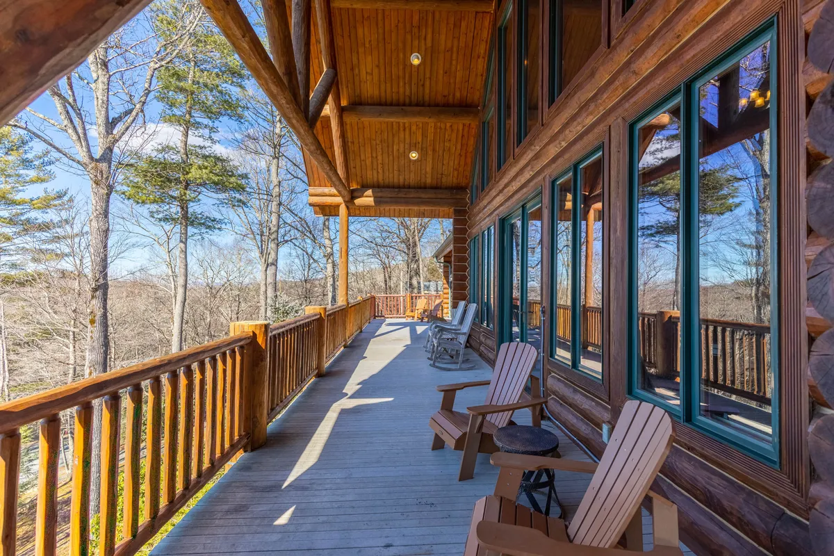 An inviting exterior view of the log cabin's porch, complete with rocking chairs, sturdy wooden railings, and panoramic vistas of the surrounding mountains. The tranquil setting is perfect for enjoying sunsets or unwinding with nature after outdoor activities.