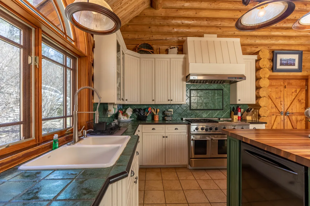 An upgraded kitchen interior featuring large windows, a green tile backsplash, wooden beams, stainless steel appliances, and a central island. The space is bright, modern, and inviting—a perfect spot for preparing and enjoying gourmet breakfasts before heading out to explore.