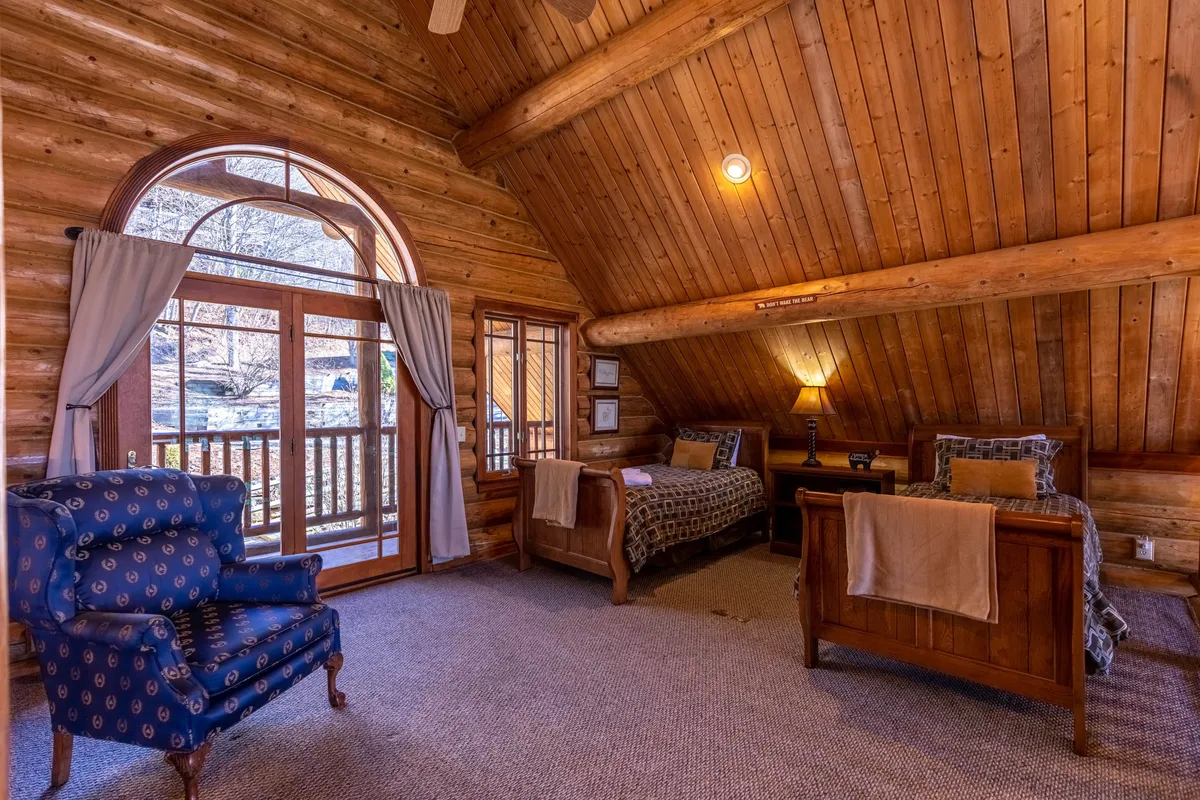 A welcoming space with wooden beams, large windows, comfortable seating, and neatly made beds. The expansive windows suggest panoramic views and natural light, providing a visual link to the surrounding mountains and outdoor thrills.