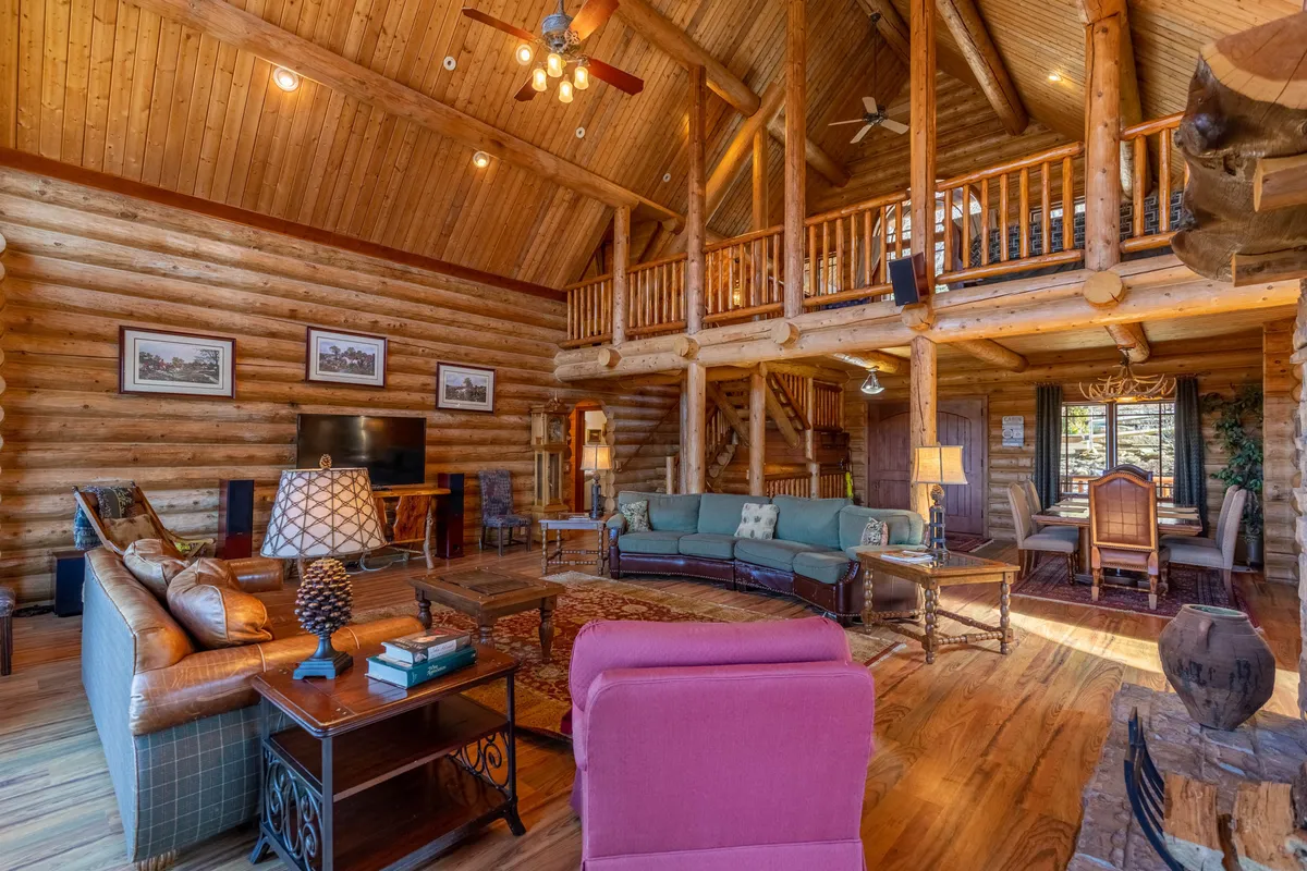 This inviting shot features the main gathering area where the living room flows seamlessly into the dining space. It showcases exposed wooden beams, a rustic staircase, comfortable seating, a large window, and a spacious dining area ideal for group meals and celebrations. The overall mood is warm and welcoming.