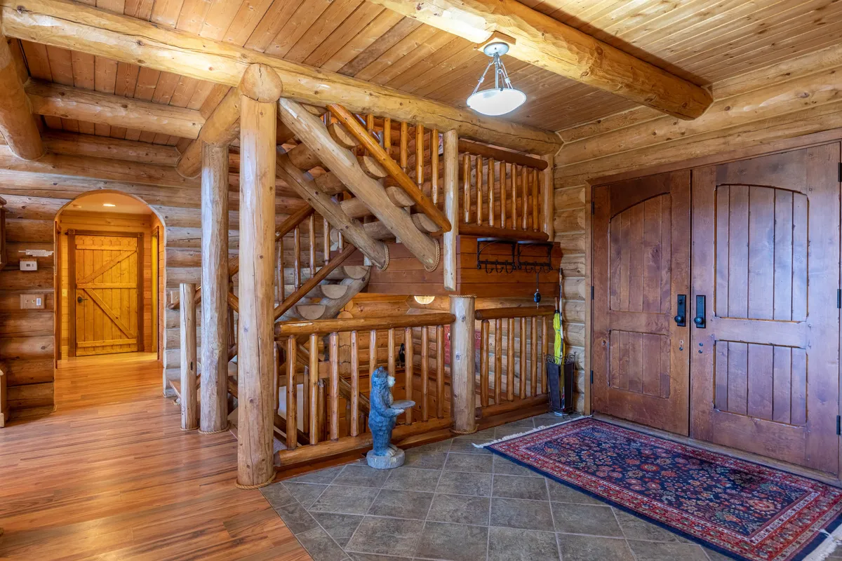 This image captures the staircase and double front doors with wooden accents, suggesting the welcoming threshold between the cozy lodge interior and the adventure-filled outdoors. The area rug and decorative statue add character and a sense of arrival, hinting at the transition from an exterior journey to the warmth of Bear Lodge.